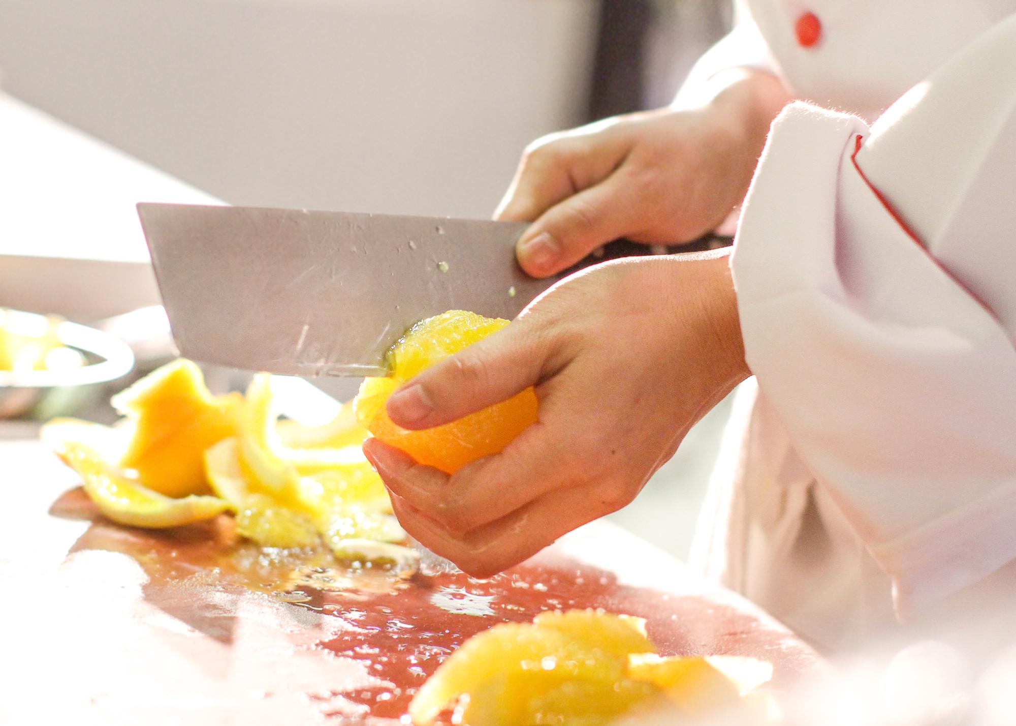 Chef slicing citrus for elegant garnish on wooden board
